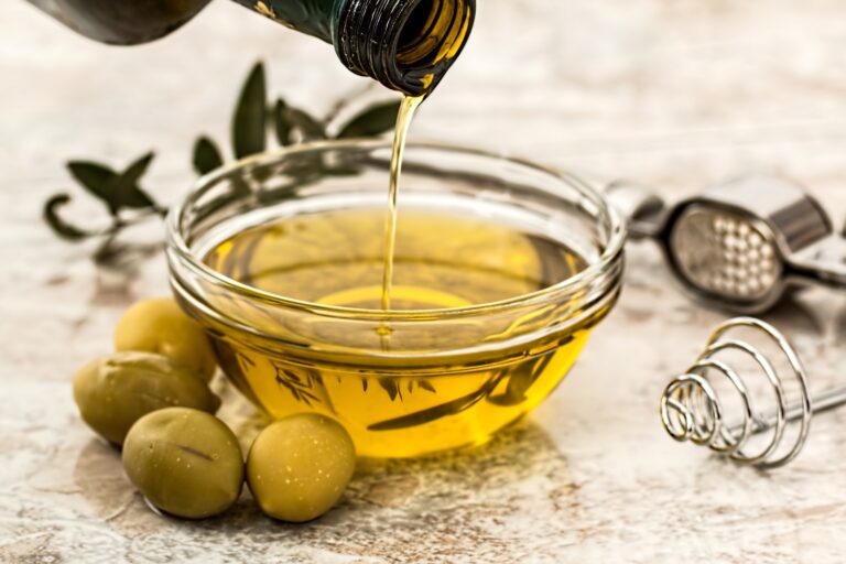 Medbest extra virgin olive oil being poured into a glass bowl with green olives and kitchen utensils on a marble surface