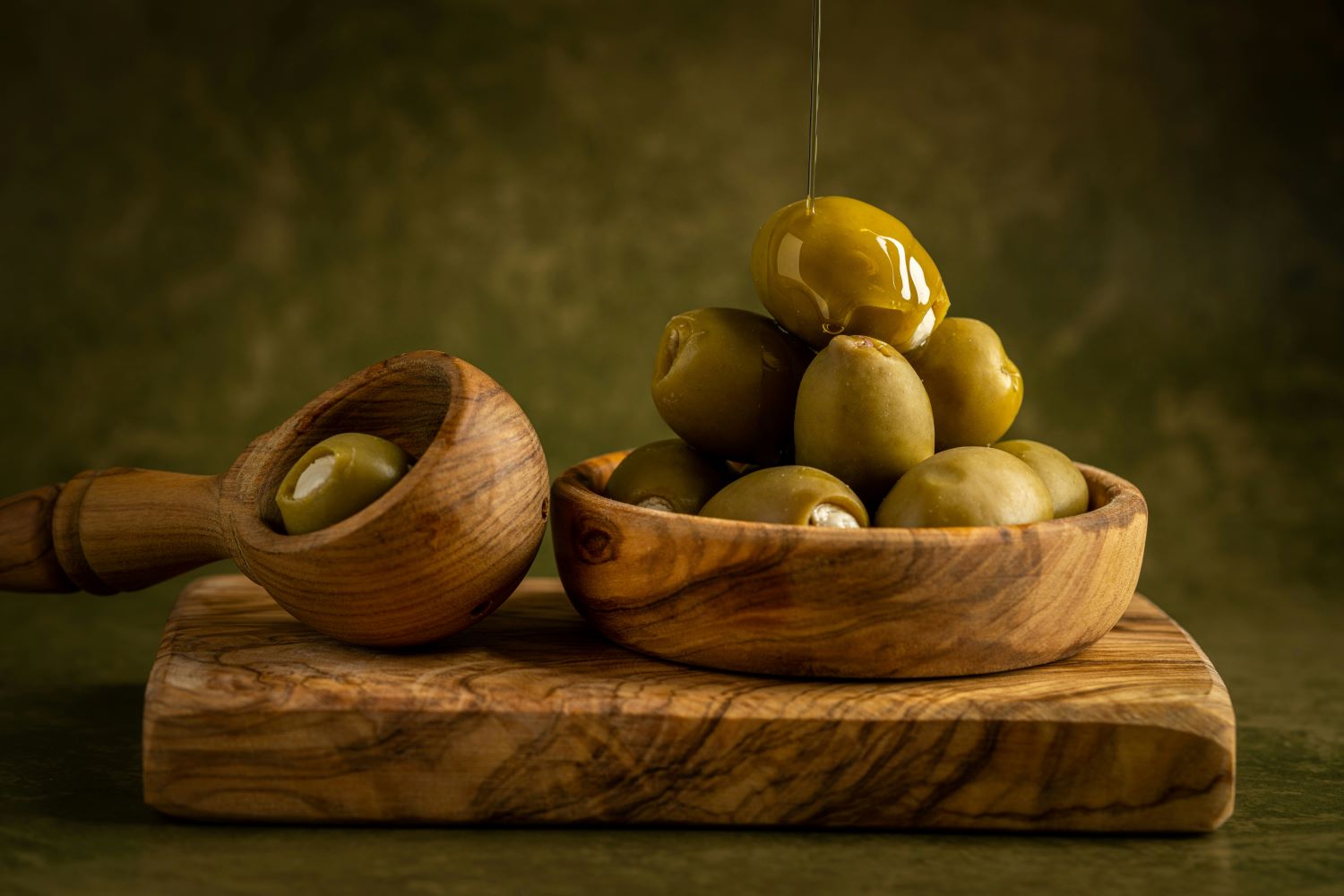 Glossy Halkidiki olives stuffed with feta cheese, drizzled with olive oil, served in wooden bowls on a rustic olive wood board
